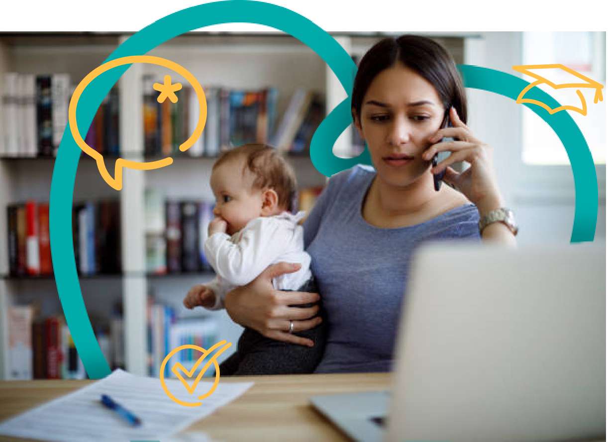 A woman is on phone in front of a laptop holding a baby. She is wearing a blue t shirt and the baby is facing away from her, with his had in his mouth.