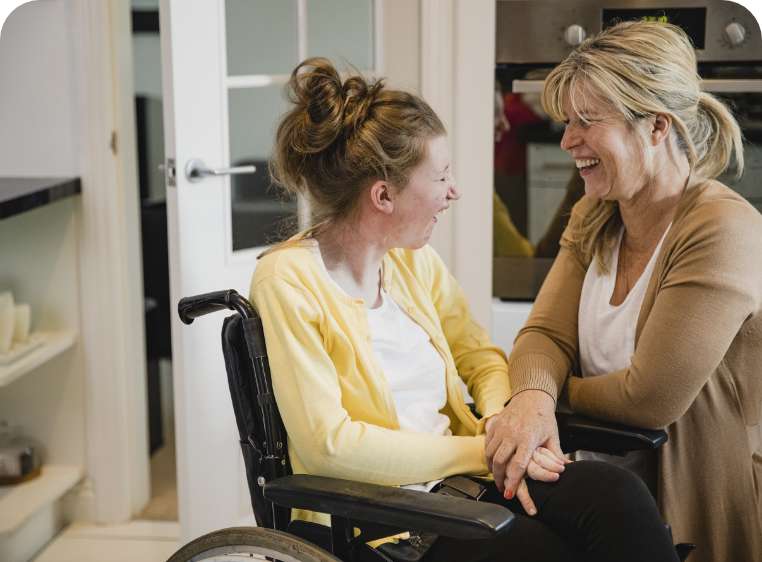 Older girl in a wheelchair smiling with her mum. She is wearing a yellow cardigan.