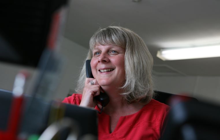 Helpline Worker Jo talking on the phone and smiling. She is wearing a red top.