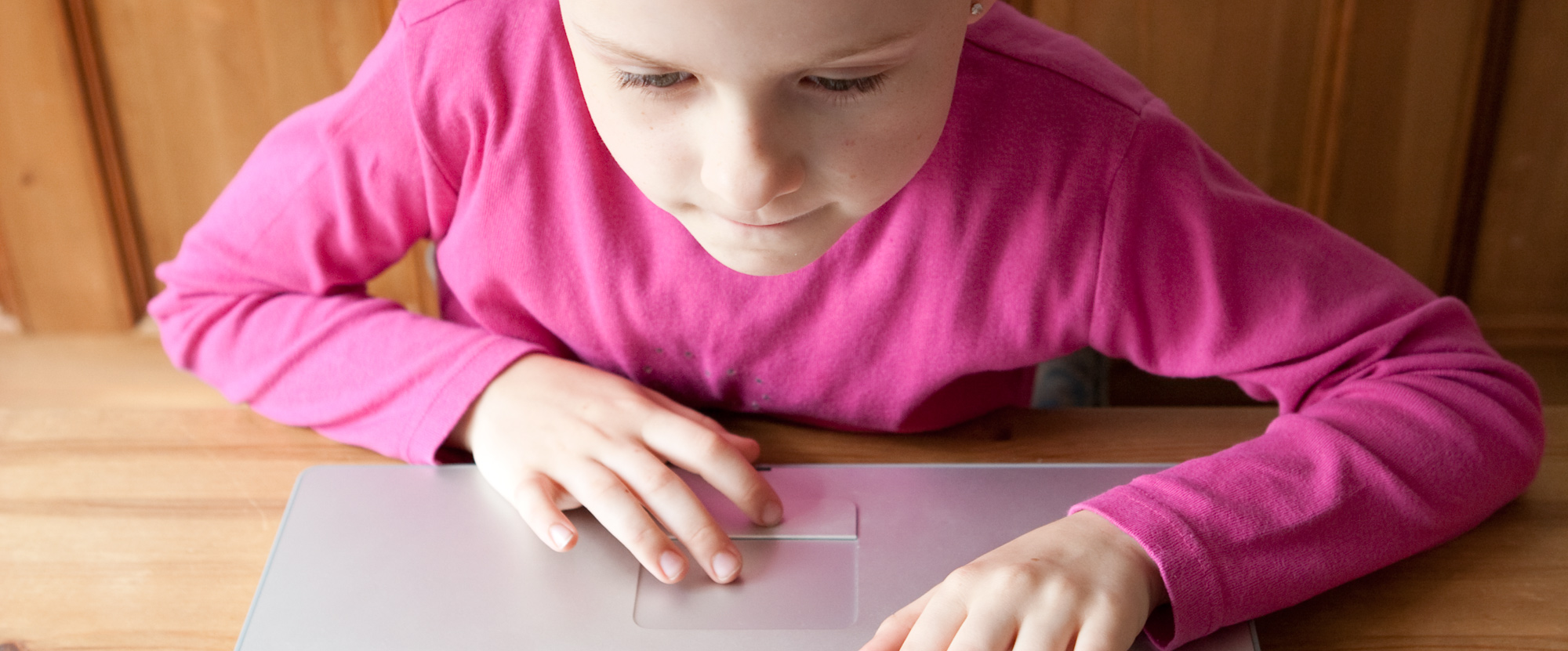 A child wearing a pink top is using a laptop, they are concentrating.