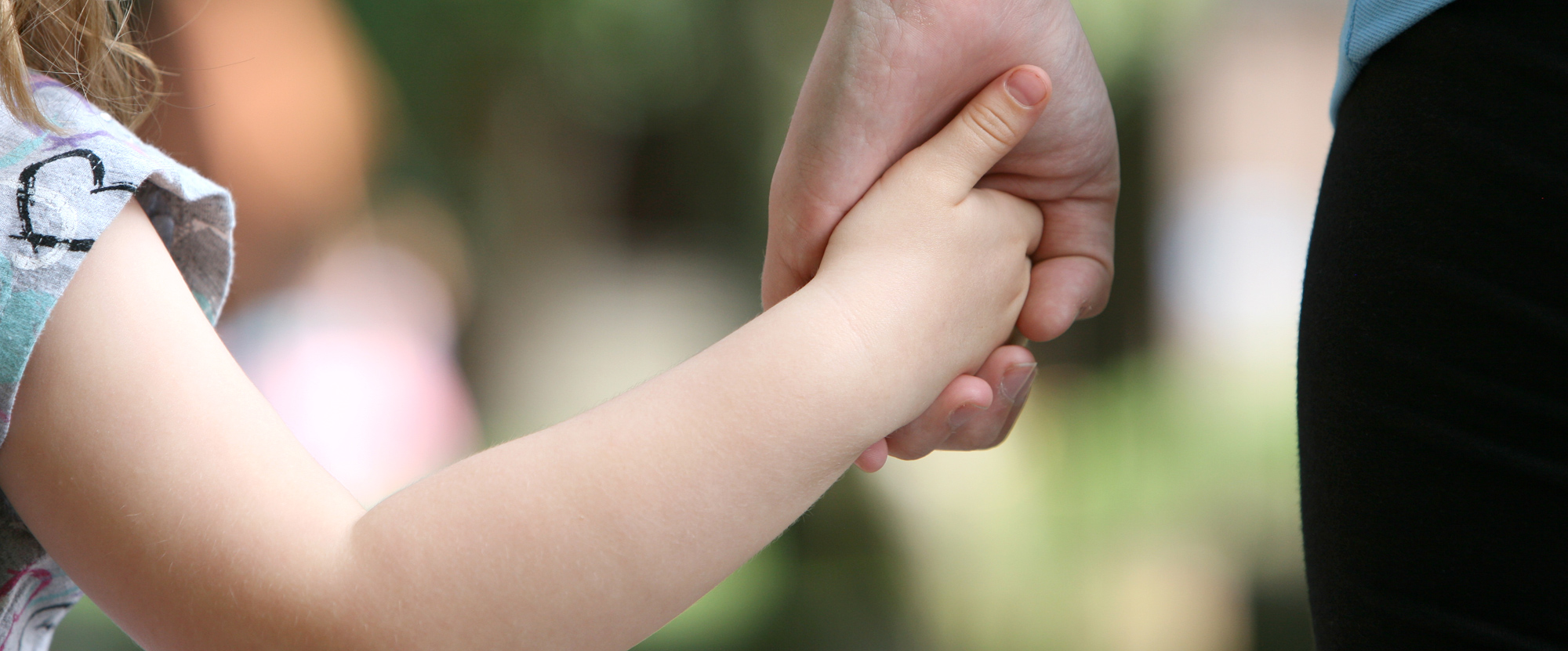A close up of a young child holding the hand of an adult.