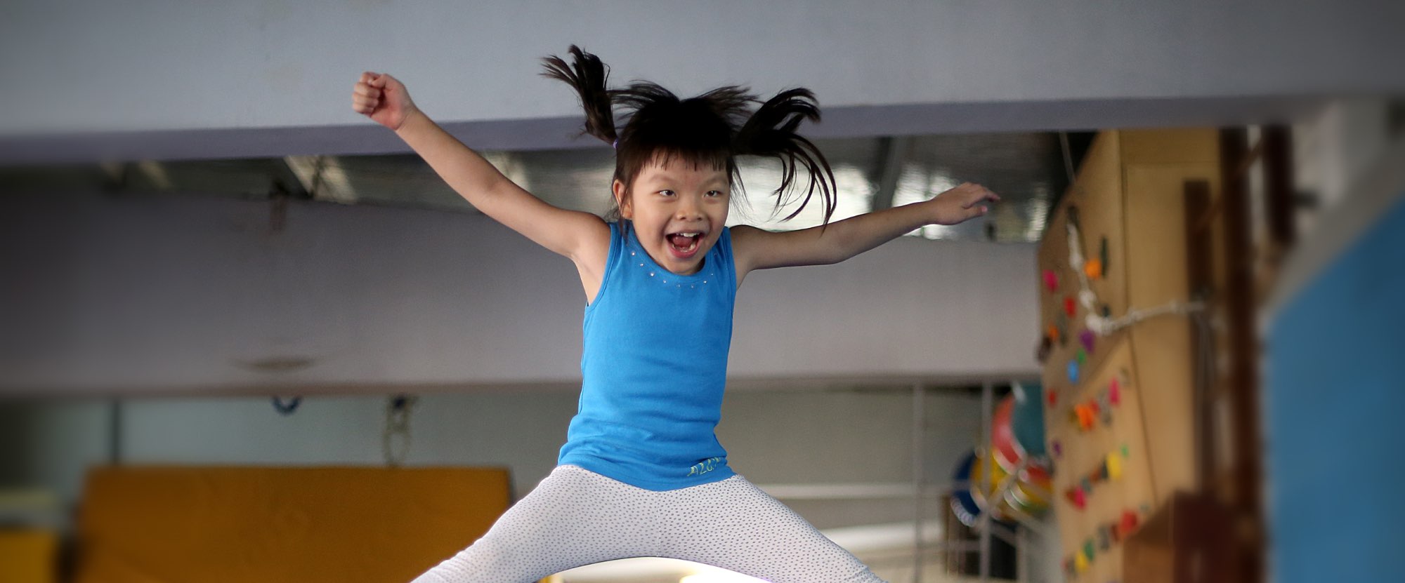 Girl in a blue t shirt doing a star jump and smiling. She has her arms outstretched.