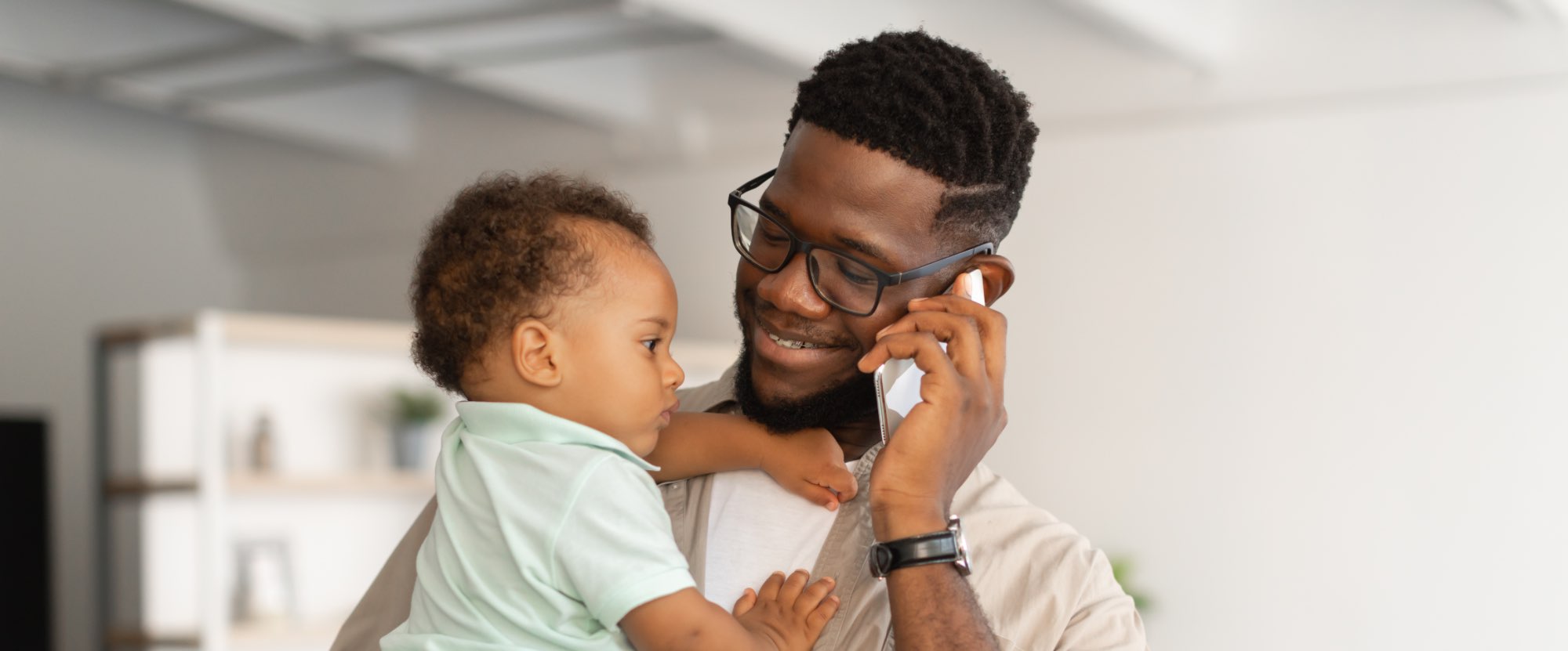 A black man on the phone, smiling and holding a small baby