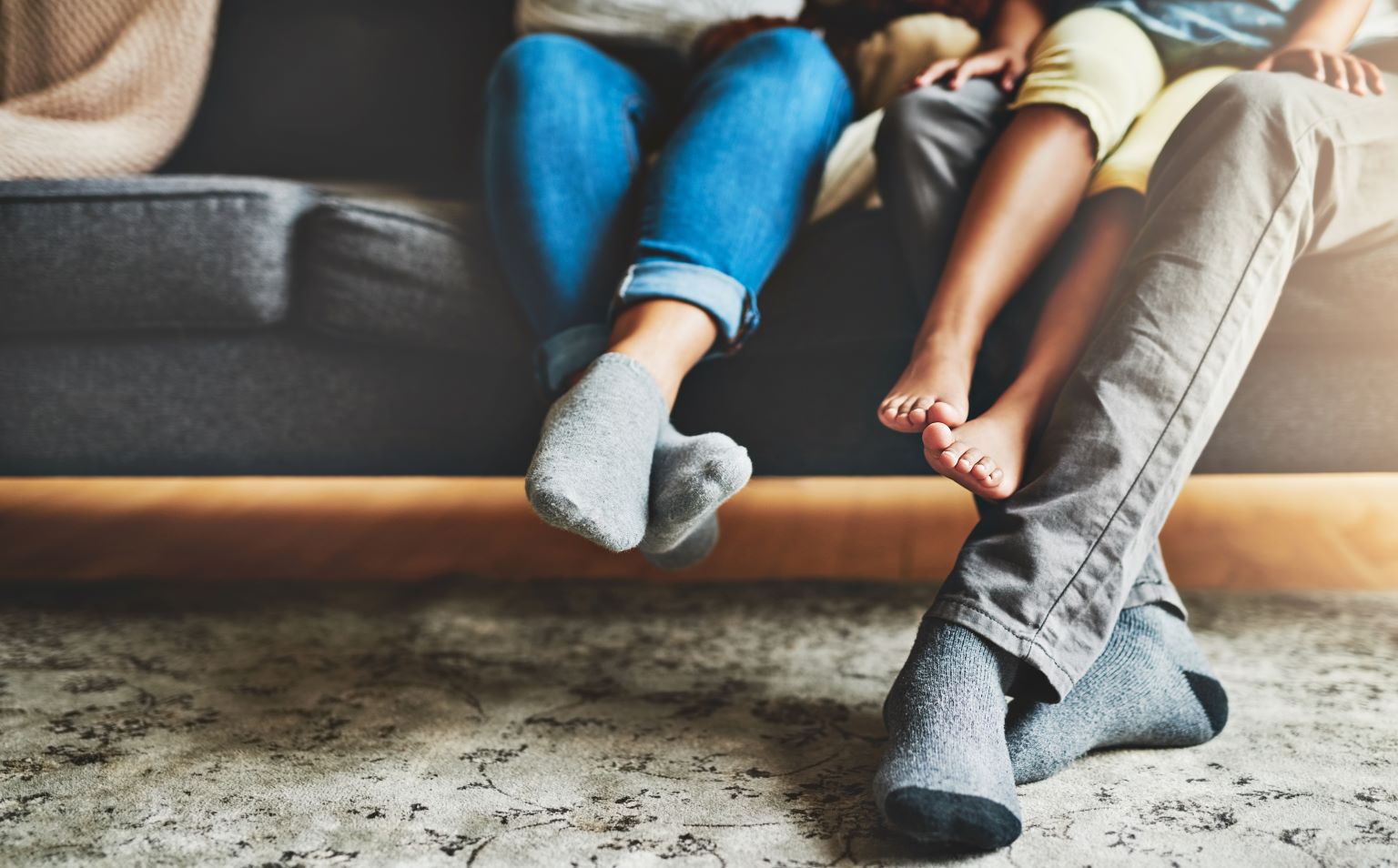 A family are sitting on a sofa, two adults and a child. With crossed legs, only their legs are in view. We can not see their faces.